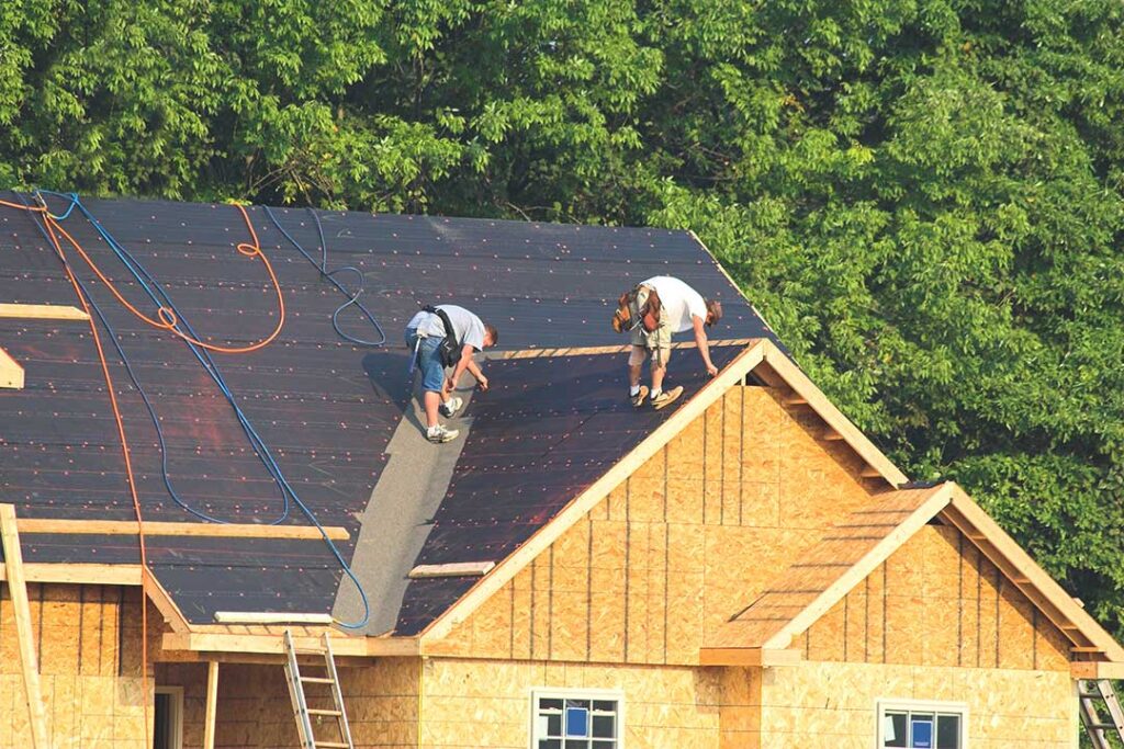 Technician inspecting a residential rooftop covered with light-colored shingles on a bright summer day.