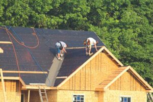 Technician inspecting a residential rooftop covered with light-colored shingles on a bright summer day.